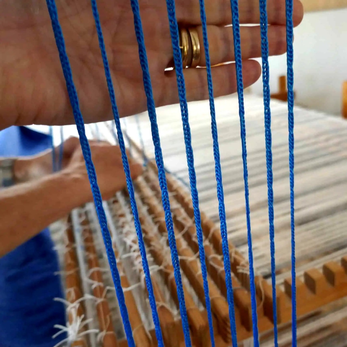 Hand hält blaue Texsolv Schlaufenschnüre vor eingesetzten Litzen – visuelle Qualitätskontrolle am Webstuhl