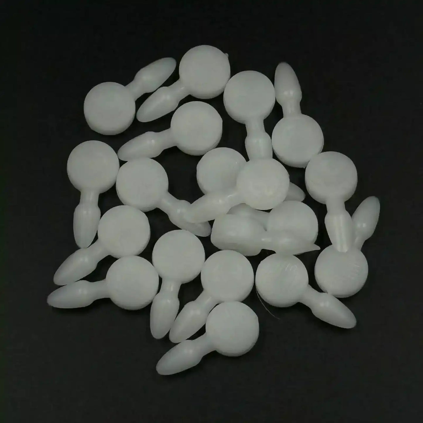 Texsolv Pfeilstecker in Weiß – runde Kunststoffstecker zur Fixierung von Texsolv Ösenschnur am Webstuhl, lose auf schwarzer Fläche verteilt