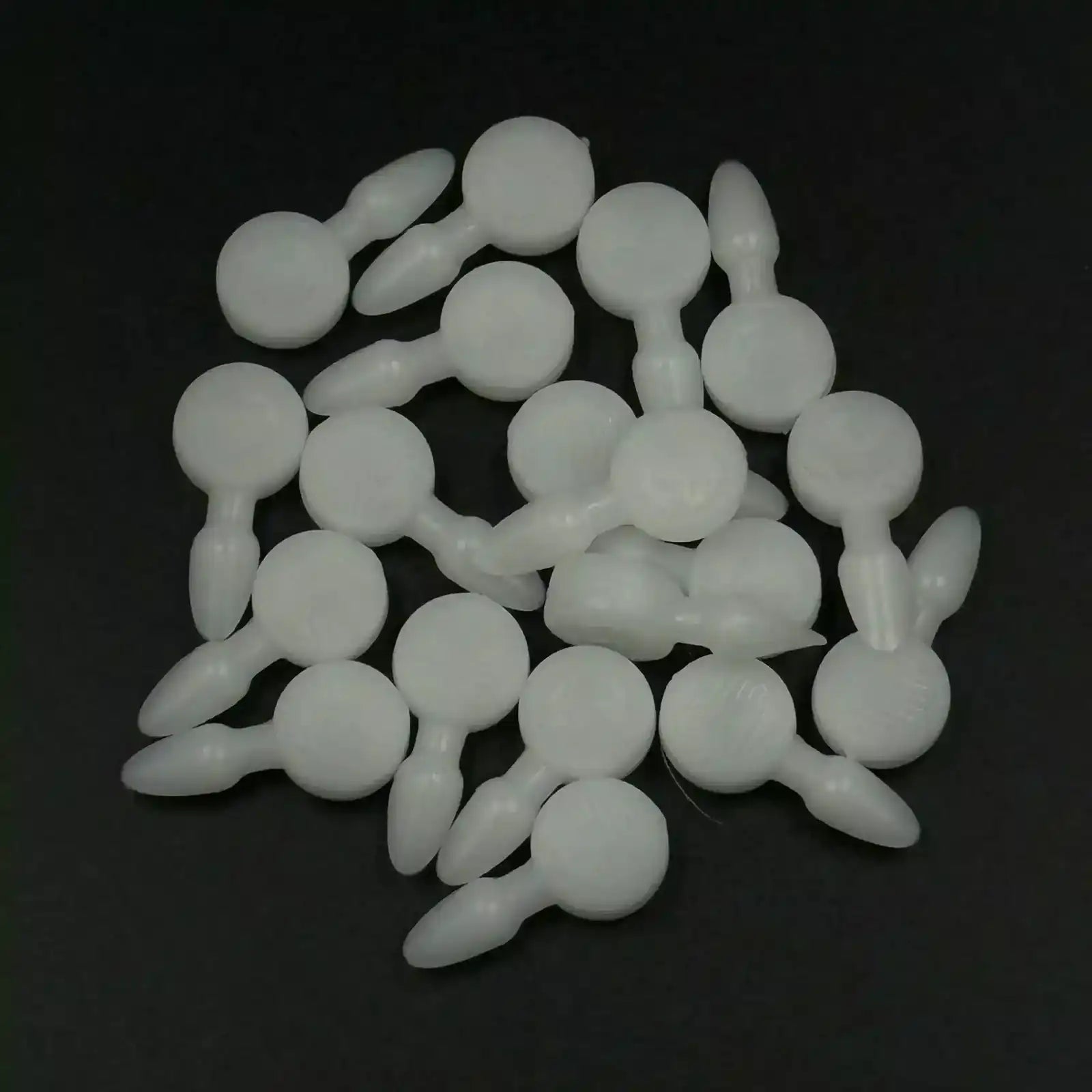 Texsolv Pfeilstecker in Weiß – runde Kunststoffstecker zur Fixierung von Texsolv Ösenschnur am Webstuhl, lose auf schwarzer Fläche verteilt