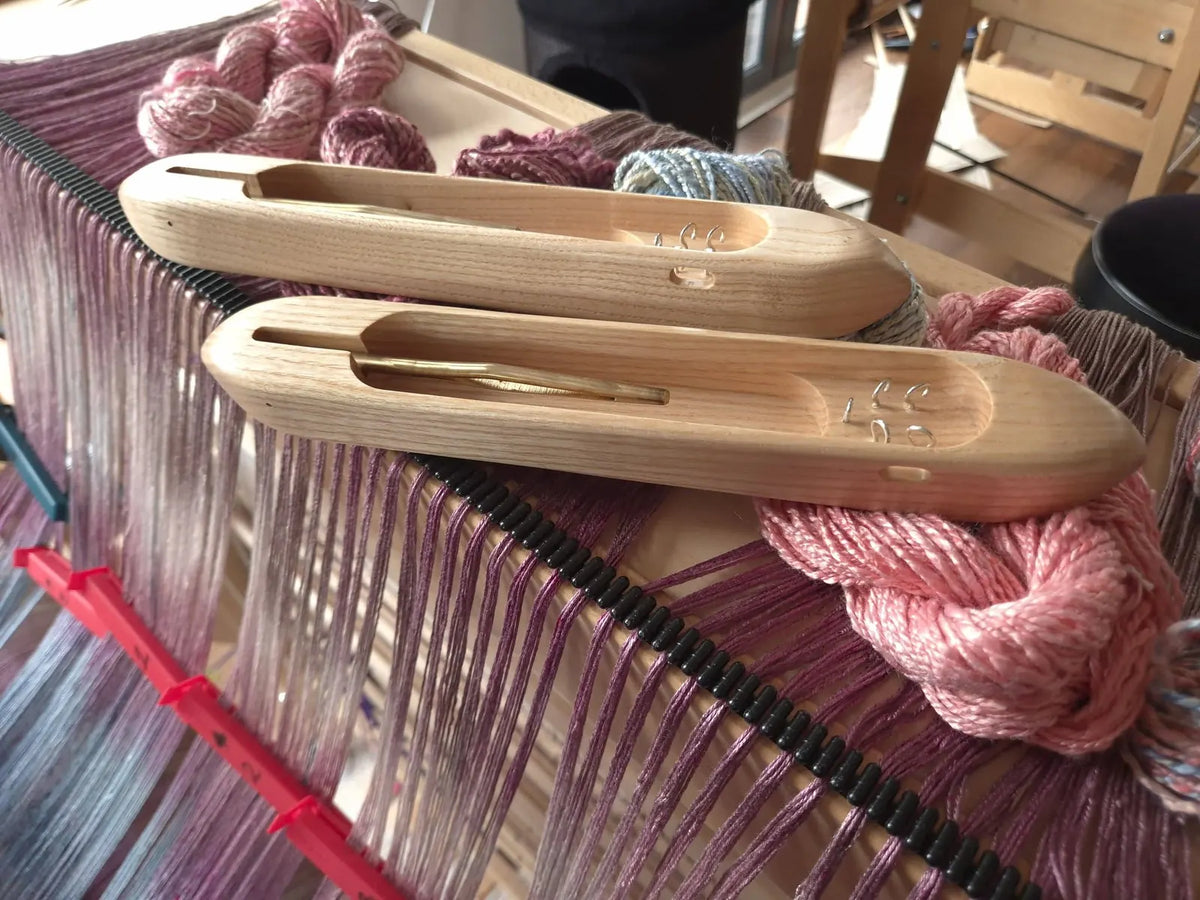 Two wooden boat shuttles on a purple warp with pink yarn during a weaving lesson